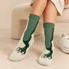 Cream crew socks featuring large green dinosaur legs and clawed dinosaur feet