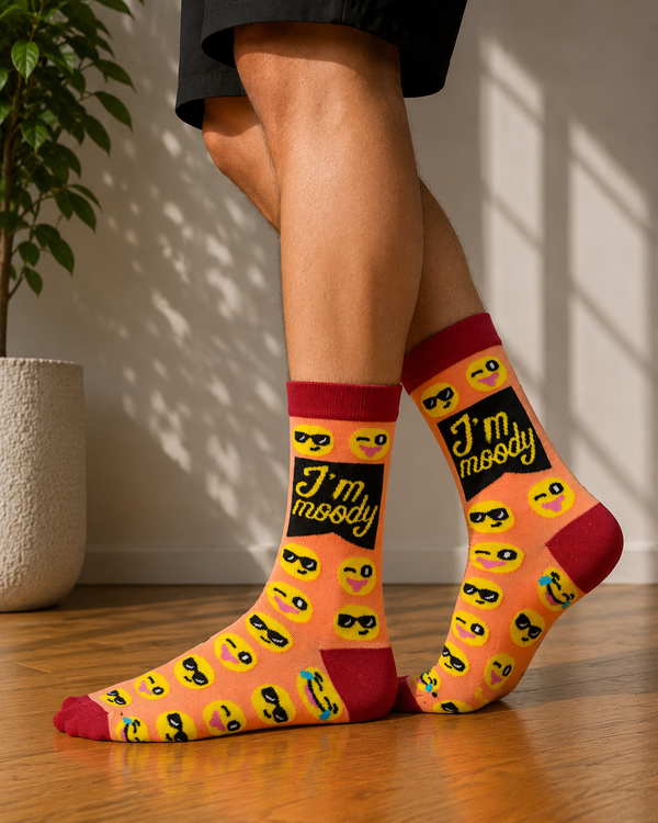 Peach-colored crew socks featuring emoji faces and the text "I'm Moody" with red heel, toe, and cuff accents.