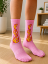 Pair of pink crew socks featuring a yellow and red flame graphic on the side, displayed on a white background.
