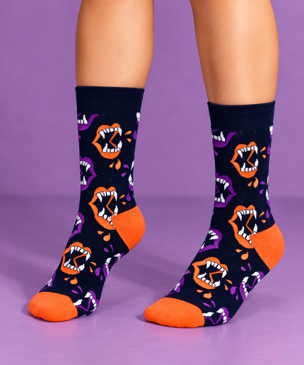 Dark navy crew socks featuring orange and purple vampire mouths with sharp white fangs, bright orange heels and toes, and a repeating spooky pattern.