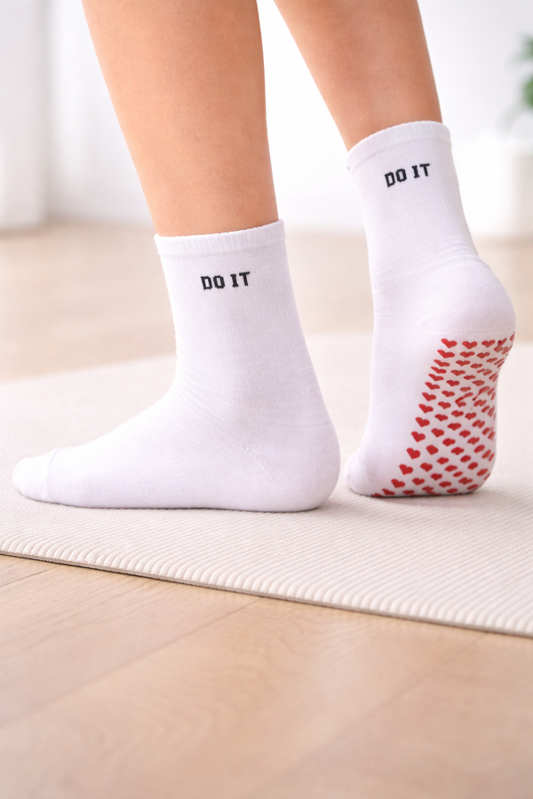 Main image: White grip socks with “DO IT” textSole image: White non-slip grip socks with red heart-shaped grips on the soleModel image: Feet wearing white non-slip grip socks on a yoga mat