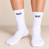 Model wearing white crew socks with bold black statement text, shown from the knees down with shoes off.