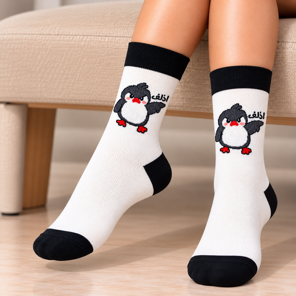 Al Taga Penguin Socks featuring a cute grey and white penguin with red feet, Arabic lettering, white fabric, and contrasting black cuffs, heels and toes.