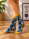 Colorful Cartoon Cat Faces Socks featuring playful cat illustrations in blue, yellow, black, and white on a blue background.