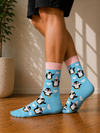 Light blue crew socks featuring cute penguins wearing winter accessories with white heart patterns.