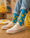 Bright blue crew socks featuring adorable yellow chick cartoon characters with playful kawaii-inspired styling and yellow toe accents.