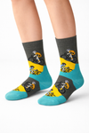 Pair of crew socks with cyclist rider pattern, dark grey base, yellow panels, and teal heel and toe on a white background.