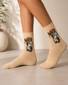 Beige crew socks featuring a Gulf-inspired falcon trainer character wearing traditional Khaleeji clothing.