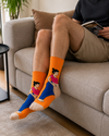 Person relaxing on a sofa wearing funny orange pregnant lady graphic socks with a cozy indoor lifestyle background.