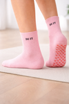 Main image: Pink grip socks with “DO IT” textSole image: Pink non-slip grip socks with red heart-shaped grips on the soleModel image: Feet wearing pink non-slip grip socks indoors
