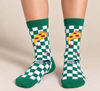Model wearing green and white checkerboard crew socks featuring pizza slice and pizza cutter graphics, shown from the knees down with shoes off.