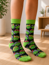 Pair of green Teenage Mutant Ninja Turtles Crew Socks featuring an all-over pattern of Leonardo, Michelangelo, Donatello, and Raphael faces on a black background.