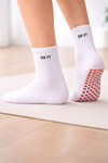 Main image: White grip socks with “DO IT” textSole image: White non-slip grip socks with red heart-shaped grips on the soleModel image: Feet wearing white non-slip grip socks on a yoga mat
