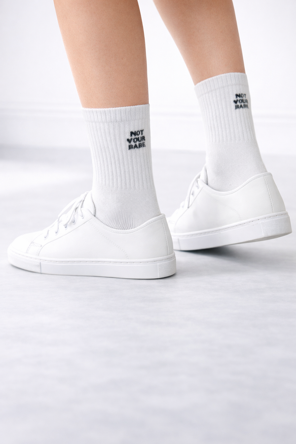White crew socks with black “Not Your Babe” text detail on a white background.