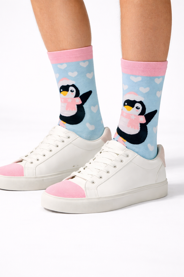 Main image: Blue crew socks with cute penguin wearing a pink scarf and white heart patternModel image: Legs wearing blue penguin heart crew socks with white sneakersClose-up image: Close-up of penguin and heart pattern on blue crew socks
